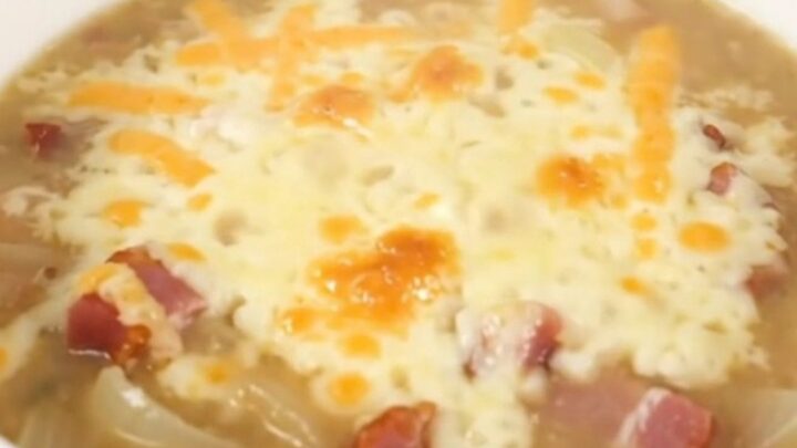 A steaming bowl of creamy onion chowder topped with melted Swiss cheese and crispy bacon bits.