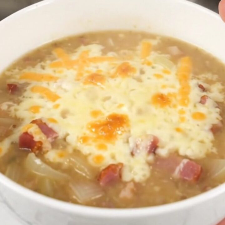 A steaming bowl of creamy onion chowder topped with melted Swiss cheese and crispy bacon bits.