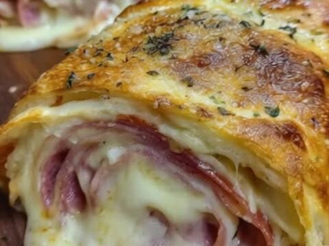 A warm, sliced stromboli roll with layers of ham, salami, and molten cheese on a rustic wooden board.