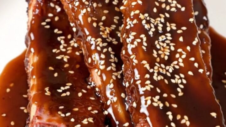 A close-up of tender, glazed baby back ribs in a slow cooker, garnished with green onions and sesame seeds.