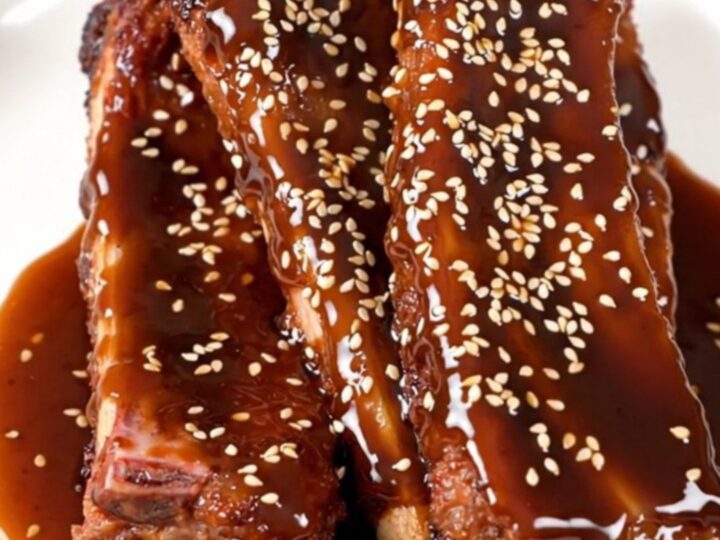 A close-up of tender, glazed baby back ribs in a slow cooker, garnished with green onions and sesame seeds.