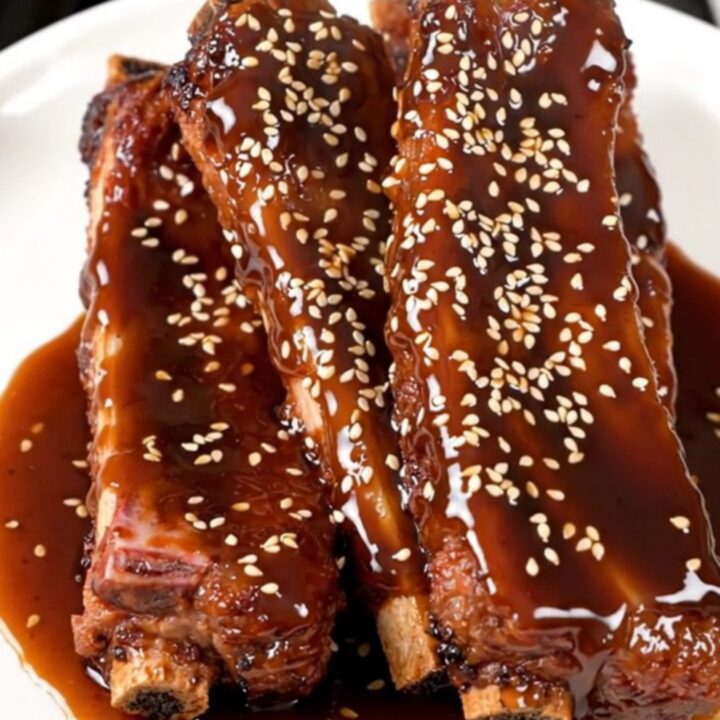 A close-up of tender, glazed baby back ribs in a slow cooker, garnished with green onions and sesame seeds.