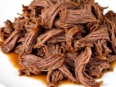 A close-up of tender, glossy mango habanero shredded beef served on a white plate.