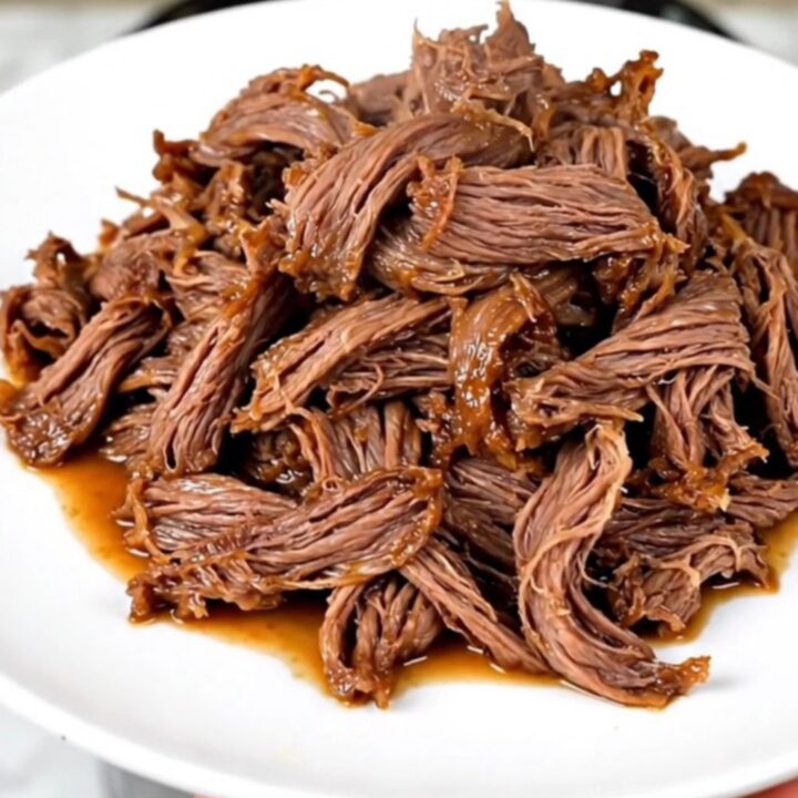 A close-up of tender, glossy mango habanero shredded beef served on a white plate.