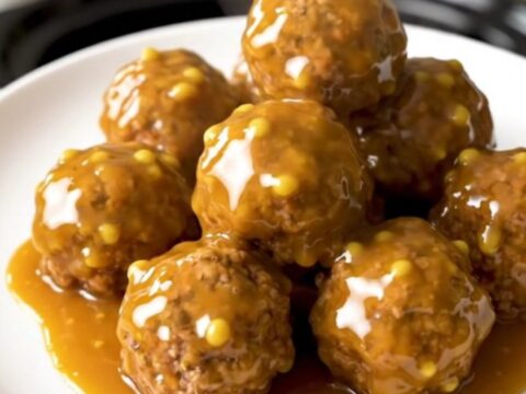 A close-up of honey mustard glazed meatballs in a black slow cooker on a white quartz countertop.