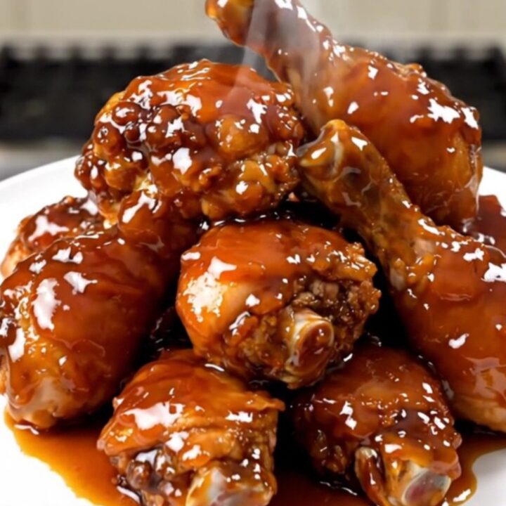 A close-up of glossy, golden-brown Cajun honey glazed chicken drumsticks served on a white plate.