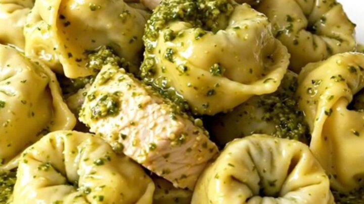 A close-up of a white plate filled with creamy pesto tortellini mixed with chicken and bacon.