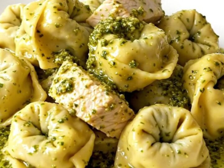 A close-up of a white plate filled with creamy pesto tortellini mixed with chicken and bacon.