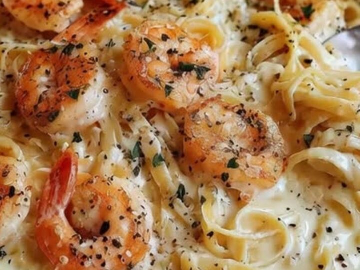 A close-up of creamy shrimp fettuccine alfredo in a dark bowl with black pepper.