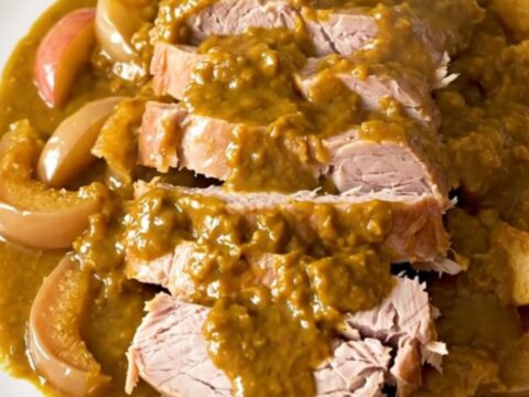 A slow-cooked pork roast topped with pumpkin butter and sliced apples on a white plate.