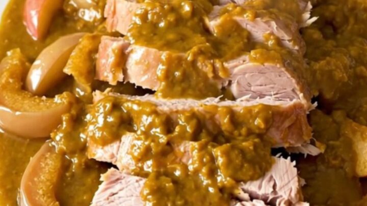 A slow-cooked pork roast topped with pumpkin butter and sliced apples on a white plate.