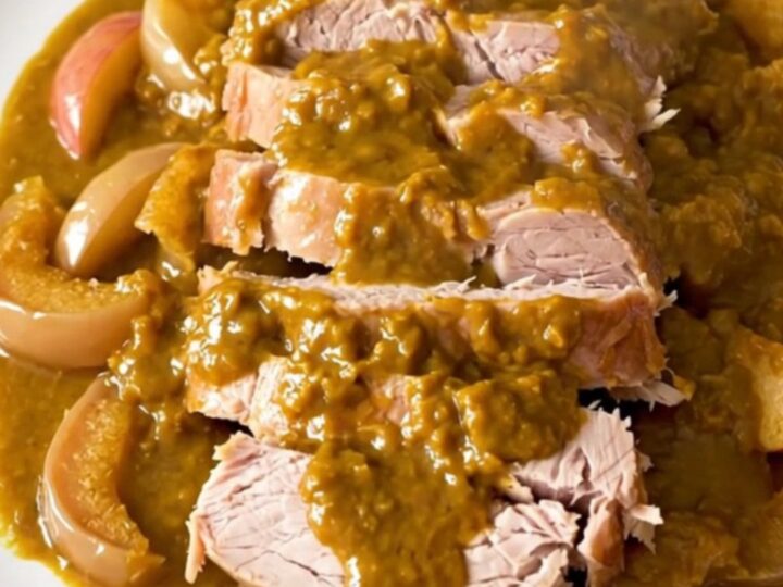 A slow-cooked pork roast topped with pumpkin butter and sliced apples on a white plate.