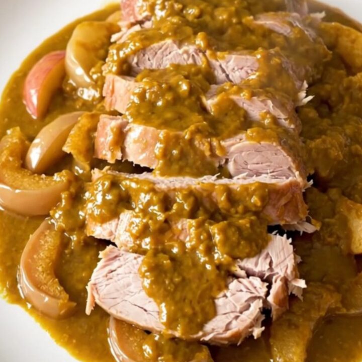 A slow-cooked pork roast topped with pumpkin butter and sliced apples on a white plate.
