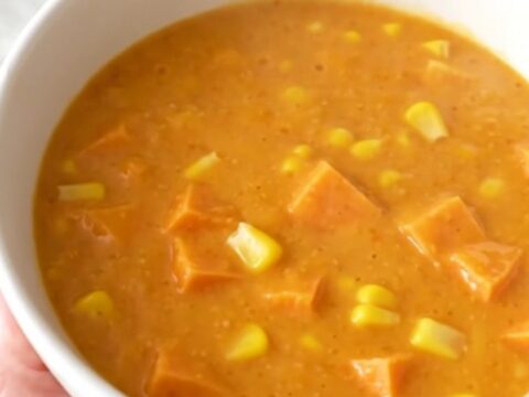 A close-up of a creamy sweet potato and corn chowder in a white bowl with steam rising.