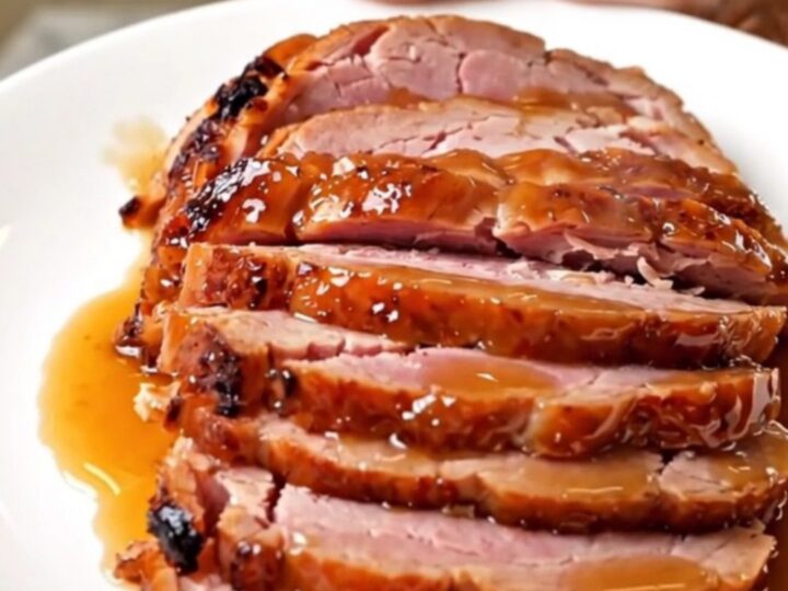 A succulent, spiral-sliced ham with a glossy, caramelized apple butter glaze on a white platter.