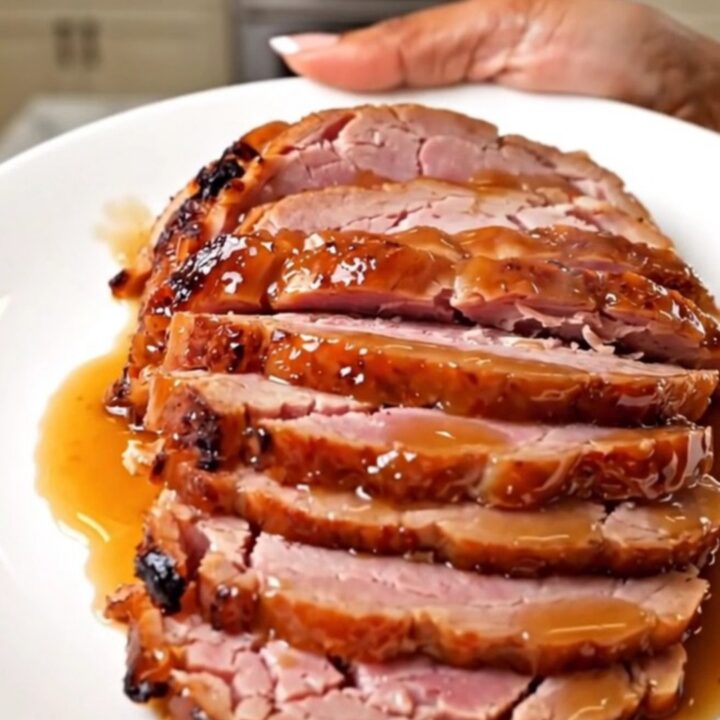 A succulent, spiral-sliced ham with a glossy, caramelized apple butter glaze on a white platter.