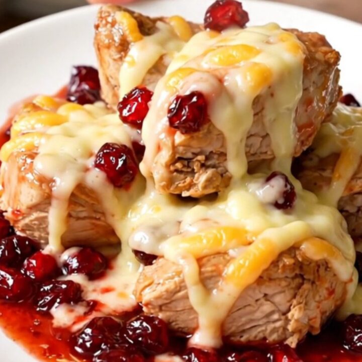 A top-down view of chicken breasts cooking in a slow cooker with cranberry sauce and onion soup mix.