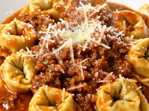 A close-up of a bowl of slow cooker tortellini bolognese topped with parmesan cheese.