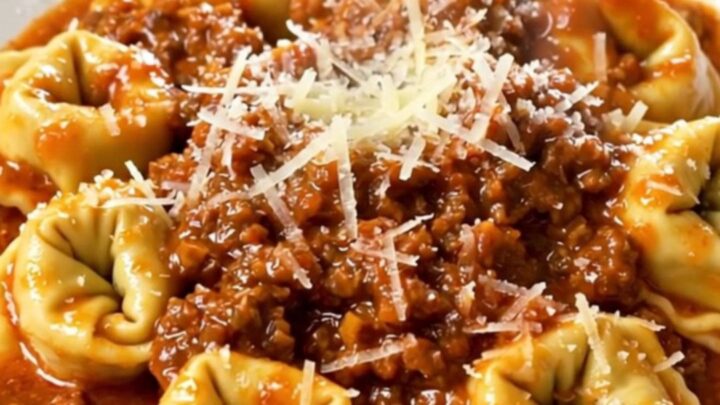 A close-up of a bowl of slow cooker tortellini bolognese topped with parmesan cheese.
