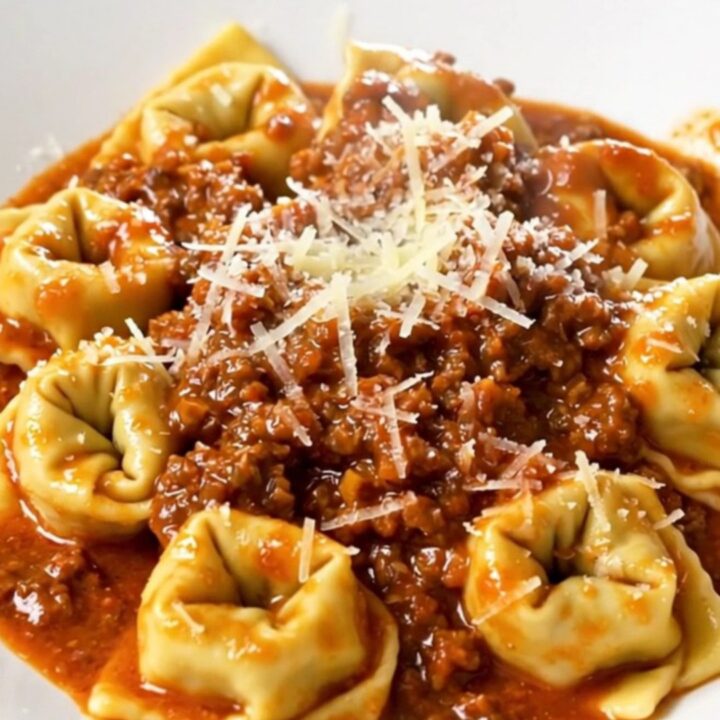 A close-up of a bowl of slow cooker tortellini bolognese topped with parmesan cheese.