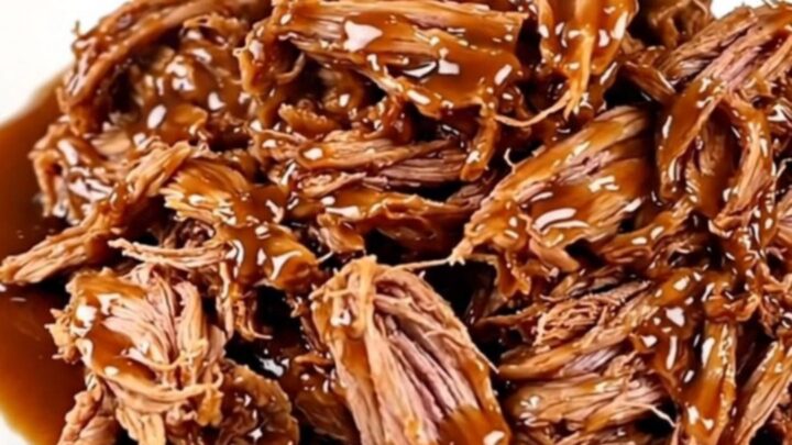 A close-up view of slow-cooked pulled pork with a glossy honey garlic glaze on a white plate.