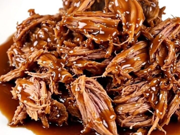 A close-up view of slow-cooked pulled pork with a glossy honey garlic glaze on a white plate.