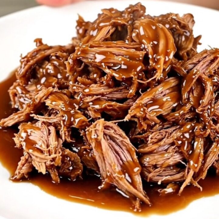 A close-up view of slow-cooked pulled pork with a glossy honey garlic glaze on a white plate.