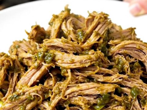 A close-up of shredded green chile pork served on a white plate with fresh cilantro.