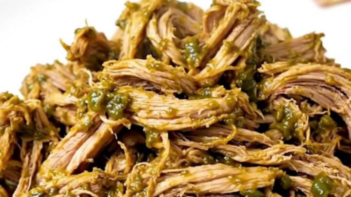 A close-up of shredded green chile pork served on a white plate with fresh cilantro.