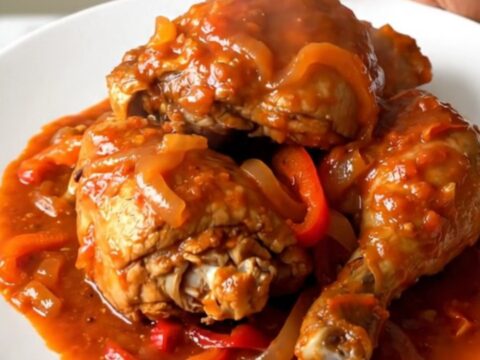 A steaming plate of slow-cooked Basque chicken with peppers and onions.