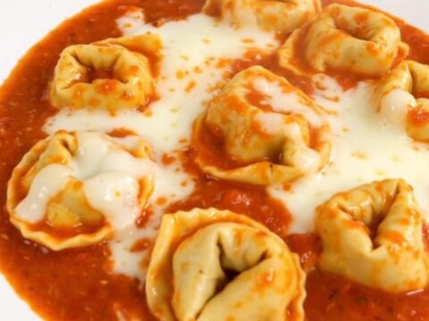 A close-up shot of a creamy tomato tortellini dish served in a white bowl.