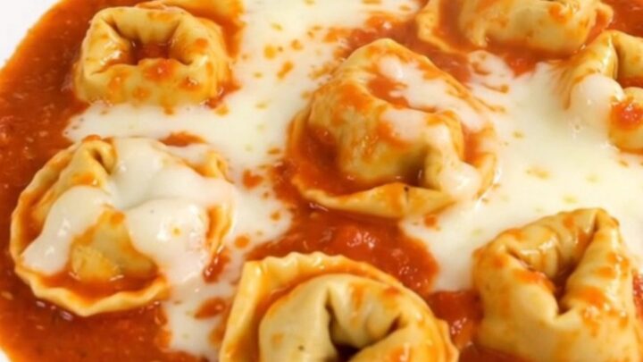 A close-up shot of a creamy tomato tortellini dish served in a white bowl.