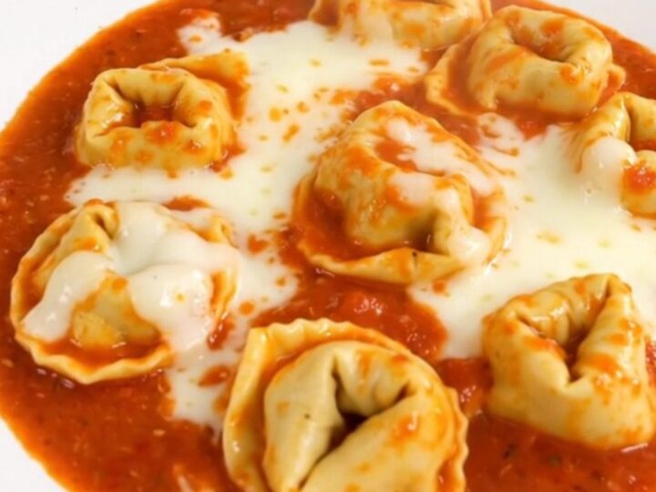 A close-up shot of a creamy tomato tortellini dish served in a white bowl.