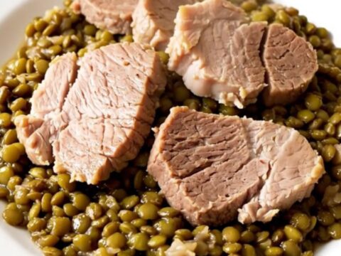 A rustic slow cooker filled with salted pork, lentils, and carrots in a bright kitchen setting.