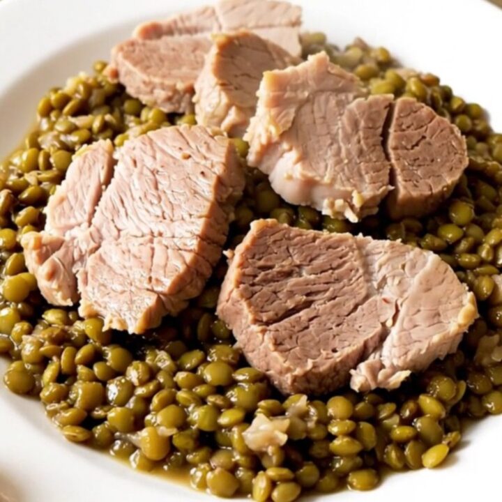A rustic slow cooker filled with salted pork, lentils, and carrots in a bright kitchen setting.