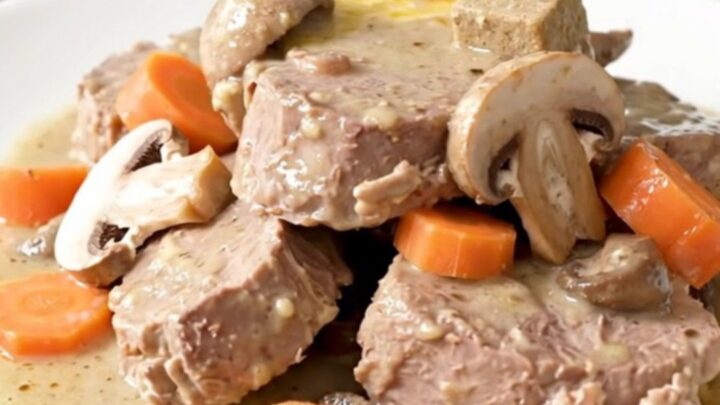 A steaming plate of creamy veal blanquette with tender meat, carrots, and mushrooms.