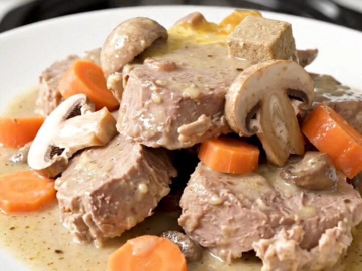 A steaming plate of creamy veal blanquette with tender meat, carrots, and mushrooms.