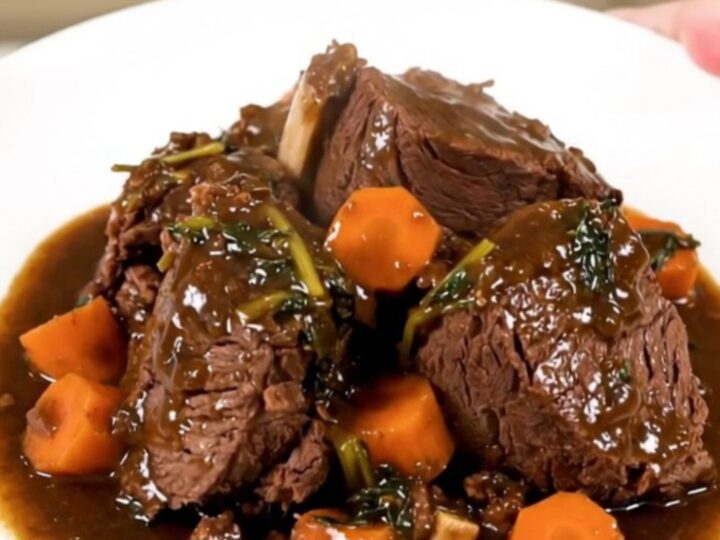 A top-down view of raw beef and carrots being added to a black slow cooker on a white quartz countertop.