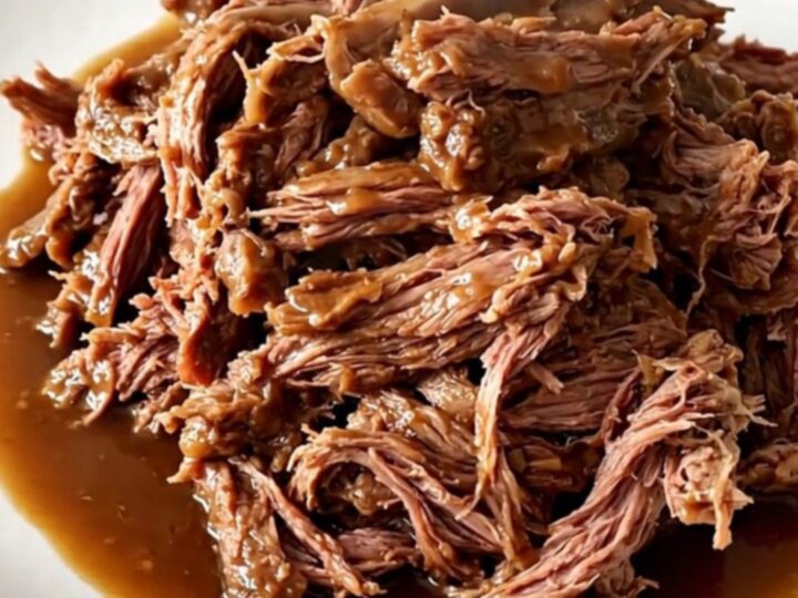 A succulent, shredded slow-cooked leg of lamb with soft carrots on a white plate.