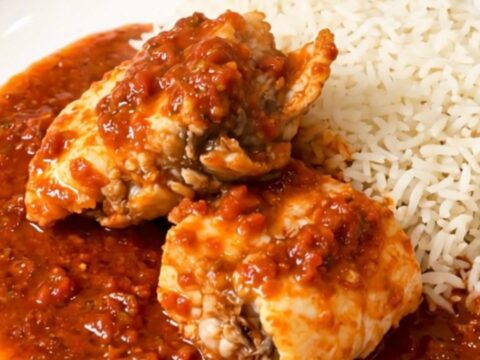 A close-up of monkfish chunks simmering in a rich tomato sauce inside a slow cooker on a quartz countertop.