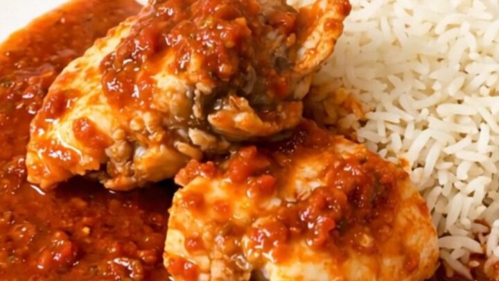 A close-up of monkfish chunks simmering in a rich tomato sauce inside a slow cooker on a quartz countertop.