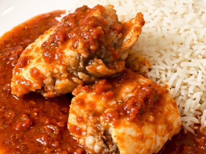 A close-up of monkfish chunks simmering in a rich tomato sauce inside a slow cooker on a quartz countertop.