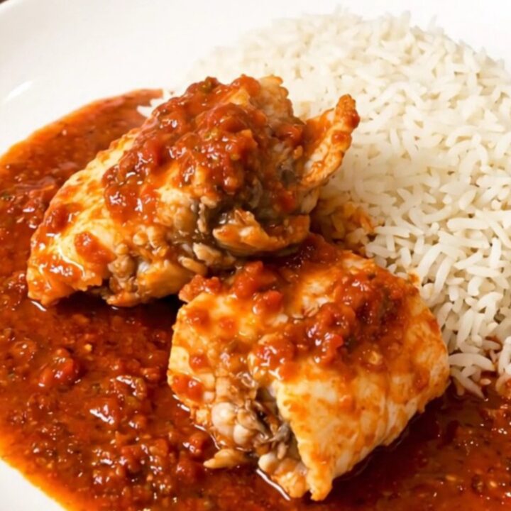 A close-up of monkfish chunks simmering in a rich tomato sauce inside a slow cooker on a quartz countertop.
