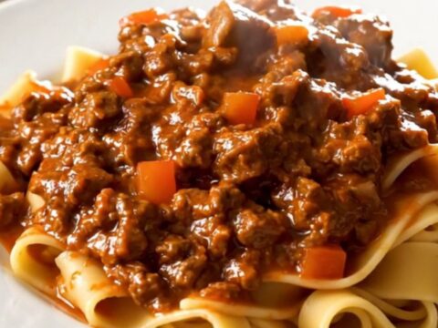 A top-down view of a slow cooker filled with raw ground beef, diced carrots, onions, and crushed tomatoes.