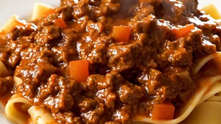 A top-down view of a slow cooker filled with raw ground beef, diced carrots, onions, and crushed tomatoes.