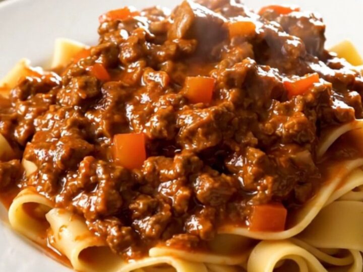 A top-down view of a slow cooker filled with raw ground beef, diced carrots, onions, and crushed tomatoes.