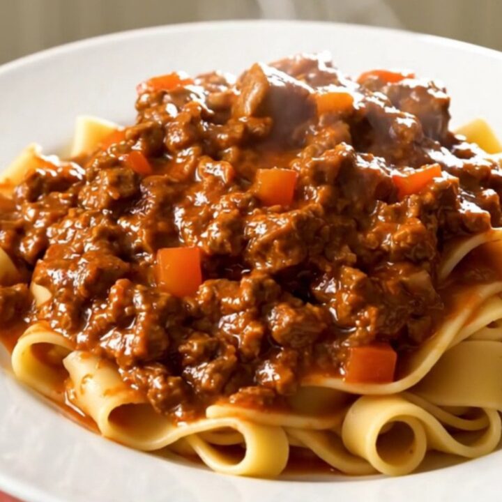 A top-down view of a slow cooker filled with raw ground beef, diced carrots, onions, and crushed tomatoes.