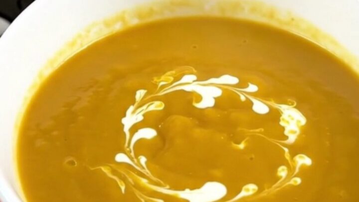 A white ceramic bowl filled with creamy orange pumpkin soup with a delicate swirl of heavy cream on top.