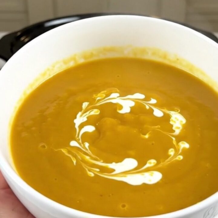 A white ceramic bowl filled with creamy orange pumpkin soup with a delicate swirl of heavy cream on top.