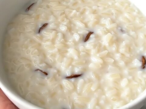 A close overhead view of creamy vanilla rice pudding inside a black slow cooker on a white quartz countertop.